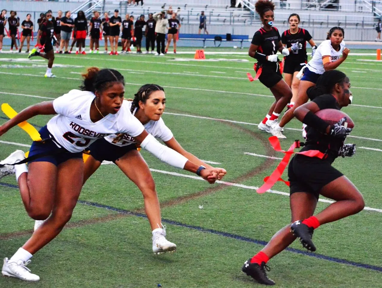 Eastvale Roosevelt’s Jai Lin Salas (23) and Melanie Lopez (center) grasp air trying to snatch Centennial’s Zion Howard’s flag during the Huskies 26 – 19 victory over the Mustangs. Credit: Photo by Gary Evans