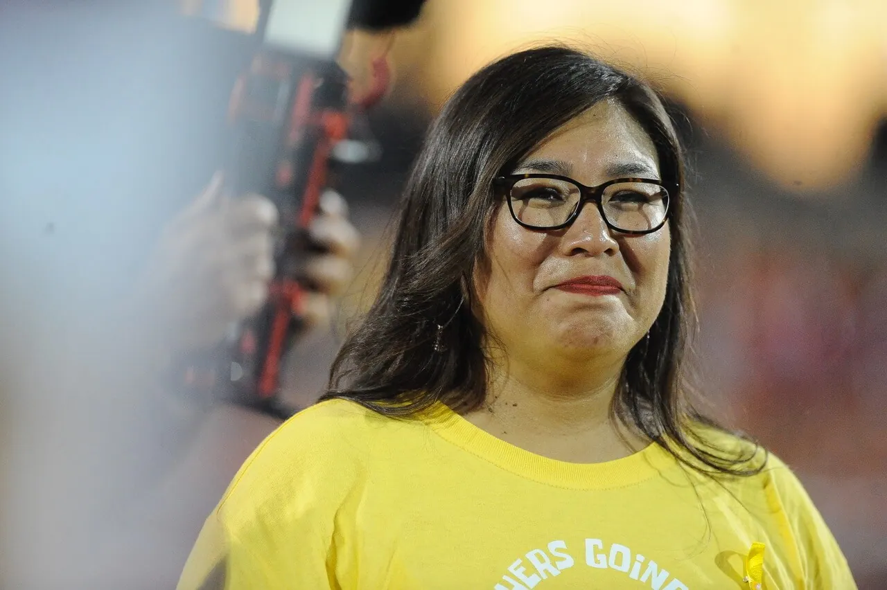 Eva Perez, a dual immersion language teacher at Corona High School, performs the ceremonial coin flip before Corona football hosted Pasadena Maranatha last week. The game was dedicated to childhood cancer victims and their families. Perez initiated the event. Families of cancer victims and survivors took part in pre-game ceremonies, wearing orange shirts while Corona players sported orange socks. 
Credit: Photo by Jerry Soifer
