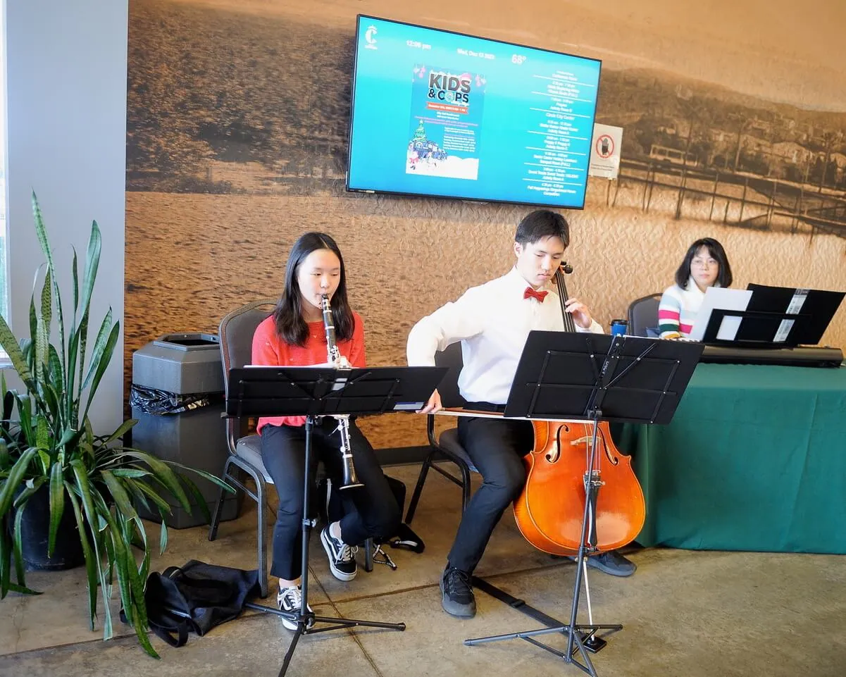 Llydia Kang, 15, left and her brother, David, 17 accompany their mother, JC, on piano, greeting guests at the Corona Senior Center holiday lunch at the Circle City Center. Credit: Photo by Jerry Soifer