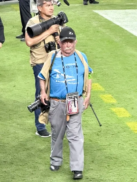 The late Jerry “Scoop” Soifer, followed by Sentinel photographer Gary Evans, walks the south end zone at the Paradise, NV, Allegiant Stadium as the Raiders take on the visiting Green Bay Packers in 2023. Besides being a giant in covering Corona-Norco High school sports for decades, Soifer was a photographer of the Raiders as the team moved from Los Angeles to Oakland and Las Vegas. Credit: Photo by Rachel Brown