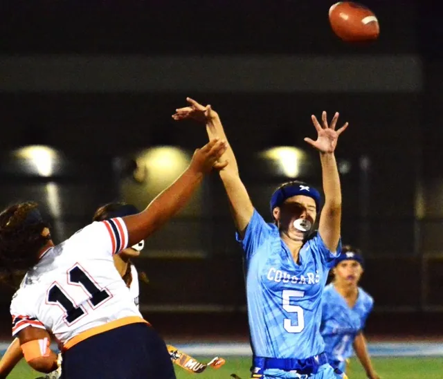 Eastvale Roosevelt QB Karissa Green (11) hand smacks the elbow of Norco’s Hayden Bolle (5) in her follow-through on a pass attempt. Green went down in pain, missing the next play, but later threw a touchdown pass leading to the Mustangs’ 18 – 13 win over the Cougars. Photo by Gary Evans