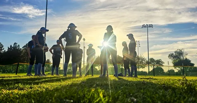 Silhouetted against the setting sun, Norco High softball players prepare for the championship game against Fullerton.